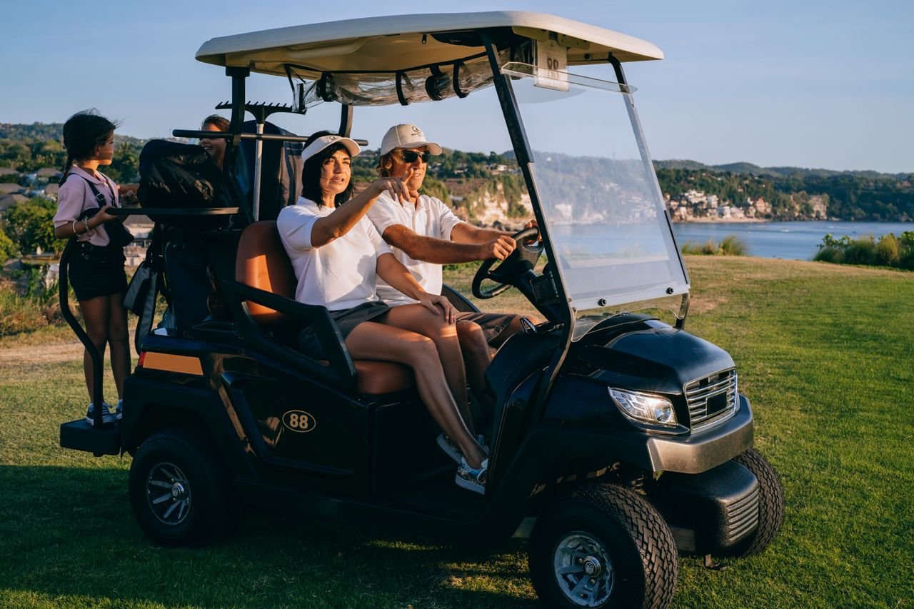 A family bonding experience captured as they ride a golf cart on a scenic golf course at sunset.