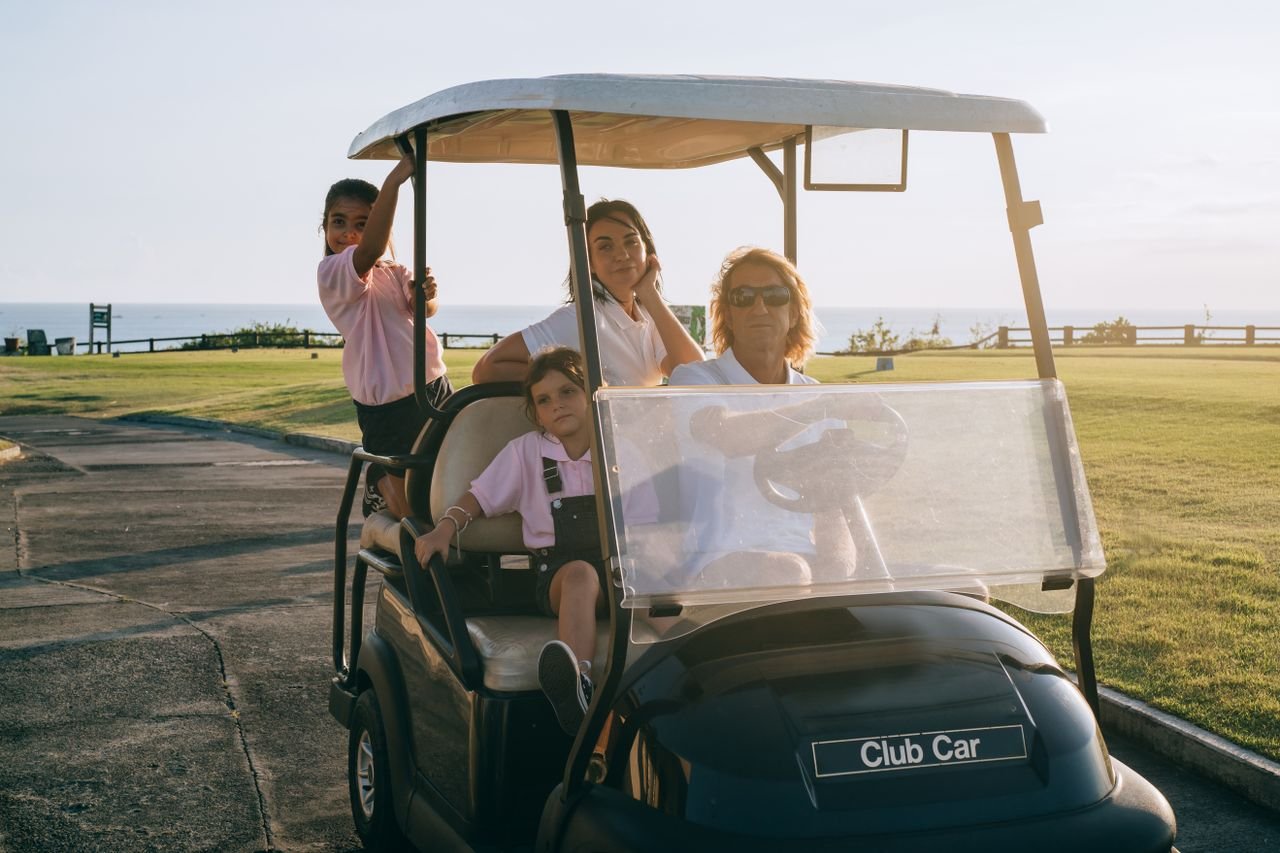 A family of four relaxing on a golf cart in a scenic outdoor setting by the sea.